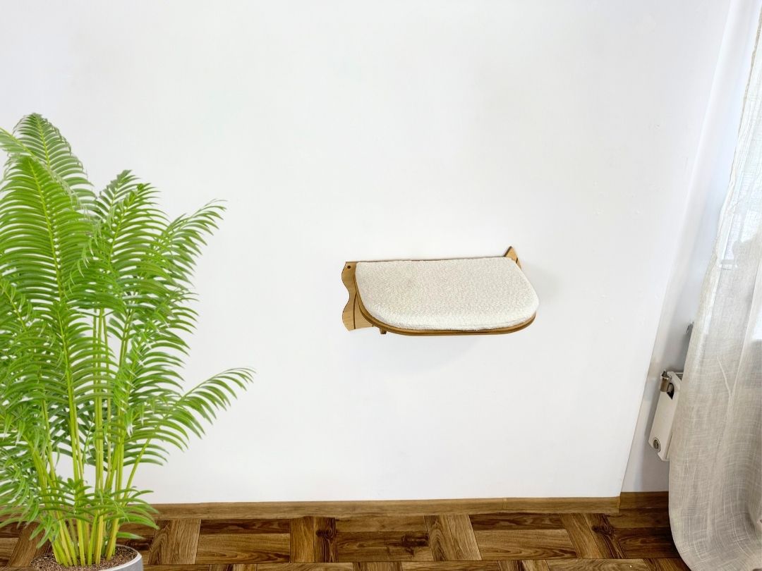 Cat wall-mounted bed against a white wall with a plant on the left.