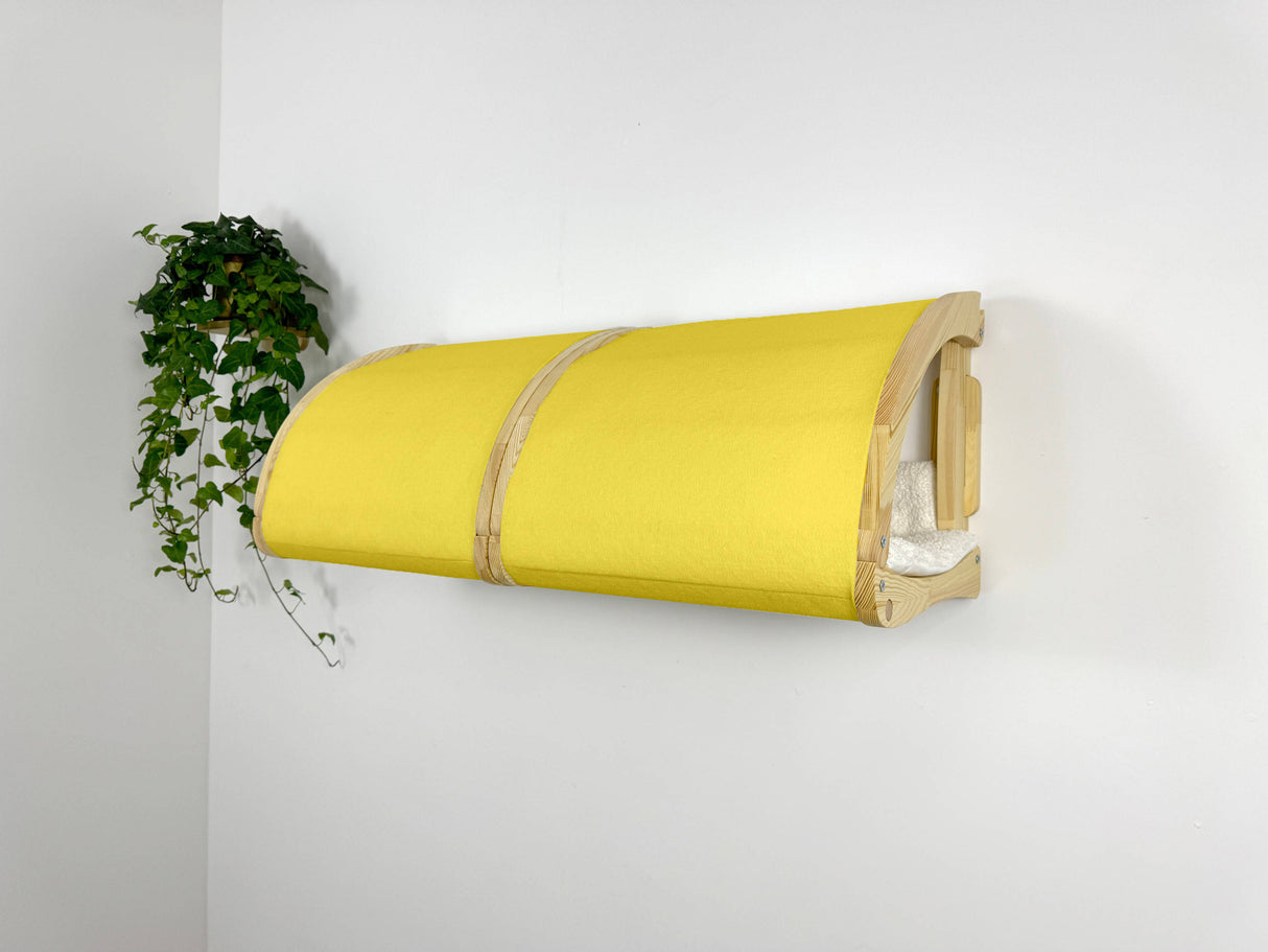 Yellow wall-mounted pet bed against a white wall with a plant on the left.