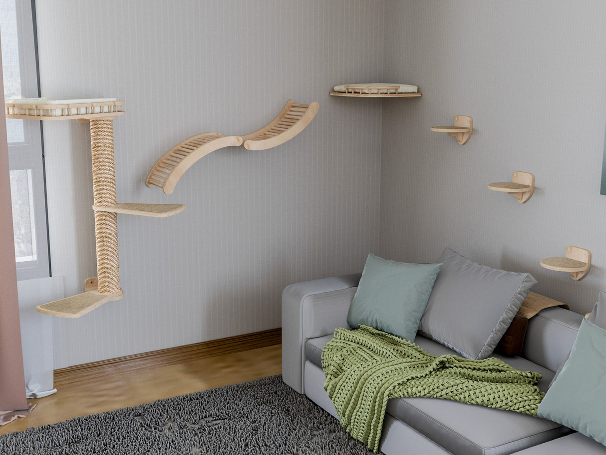 Cat tree with shelves on a wall next to a gray sofa with cushions and a green blanket.