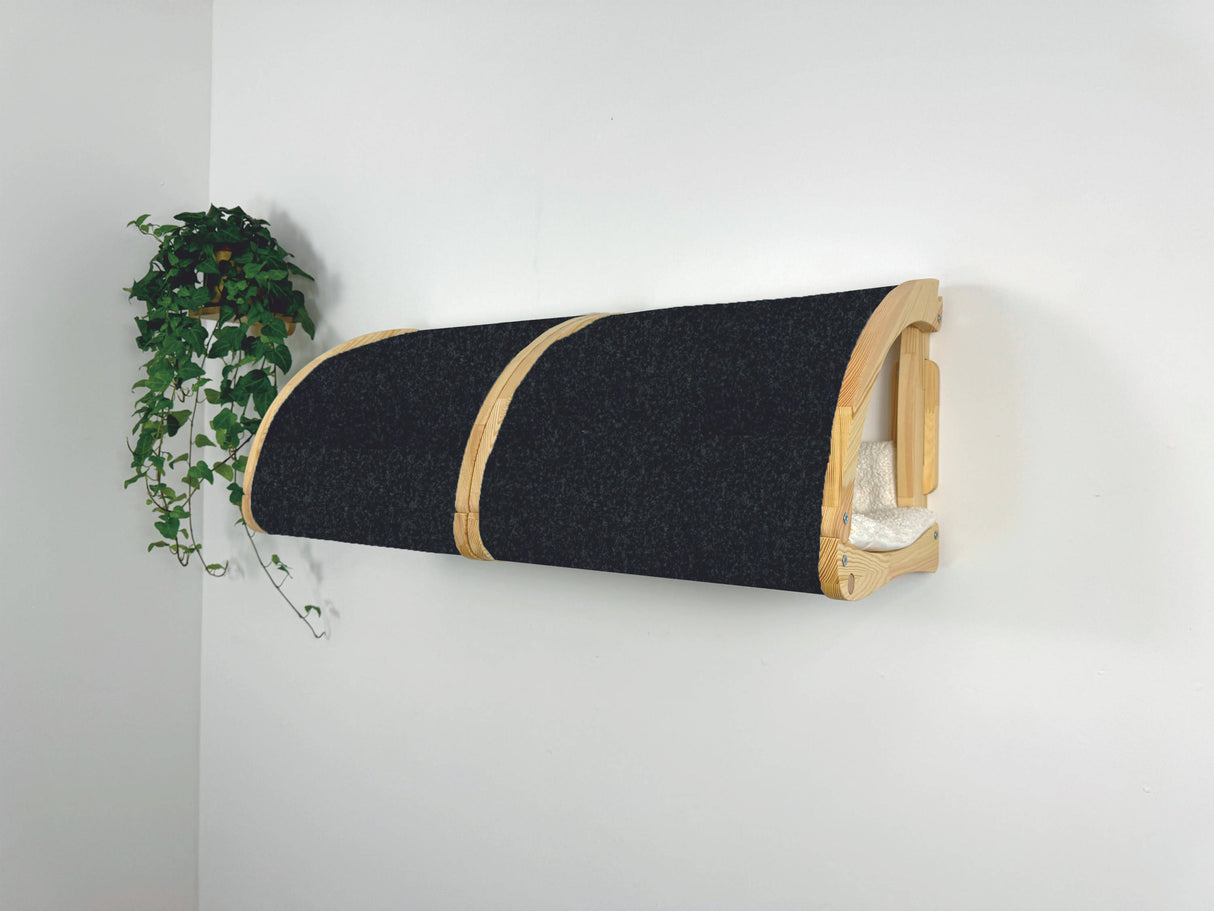 Wall-mounted cat bed with black cushion and wooden frame against a white wall.