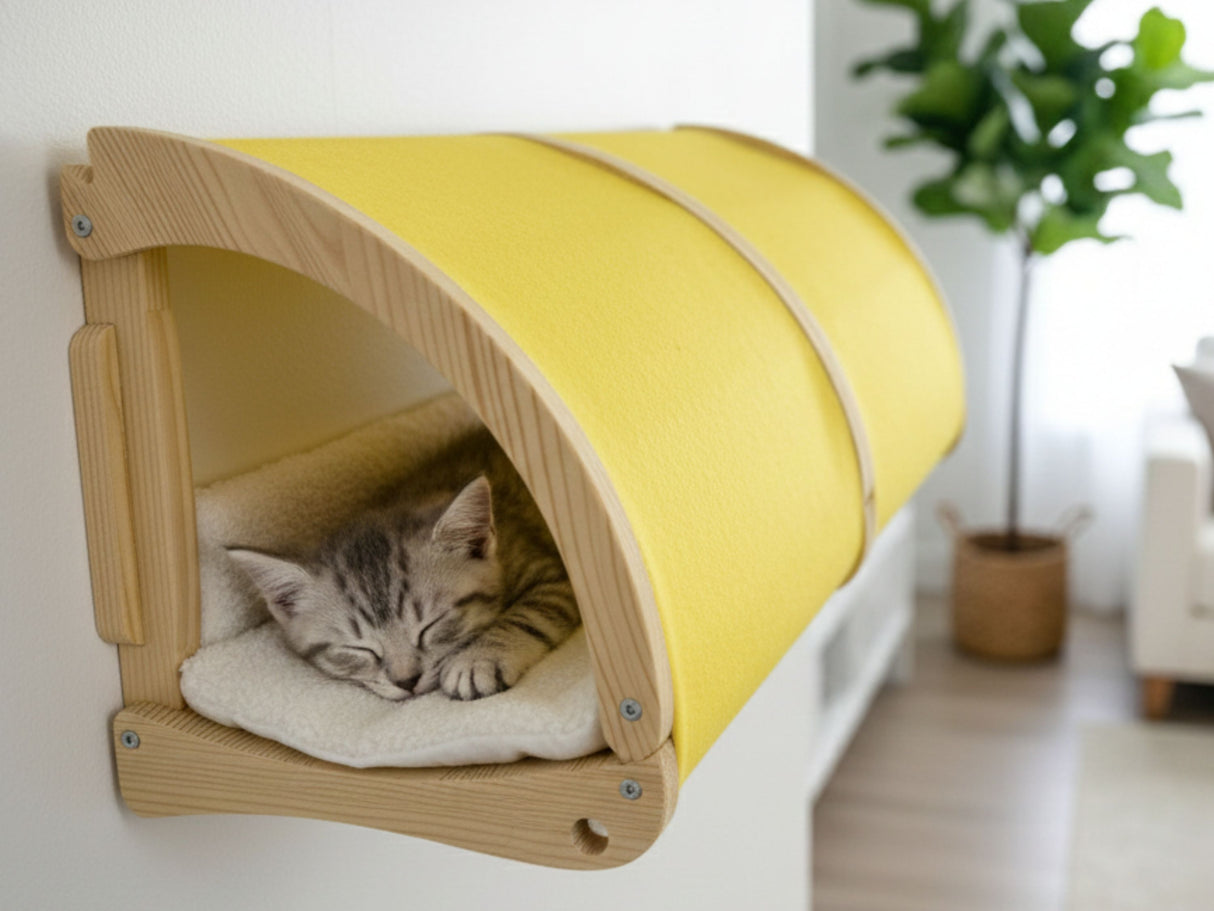 Cat lying in a yellow and wooden pet bed in a room with a plant and furniture.
