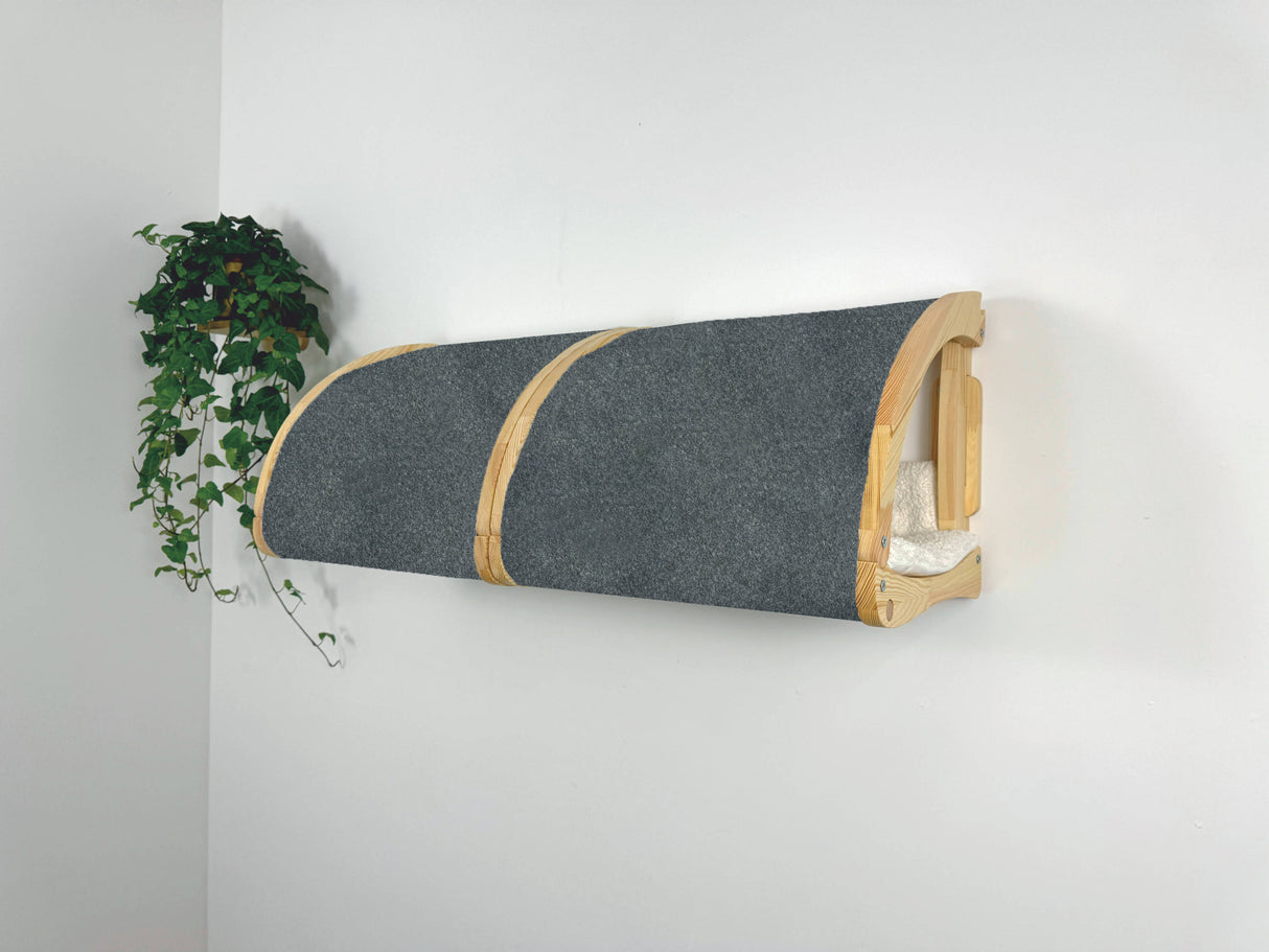 Wall-mounted cat bed with wooden frame and gray cushion on a white wall.