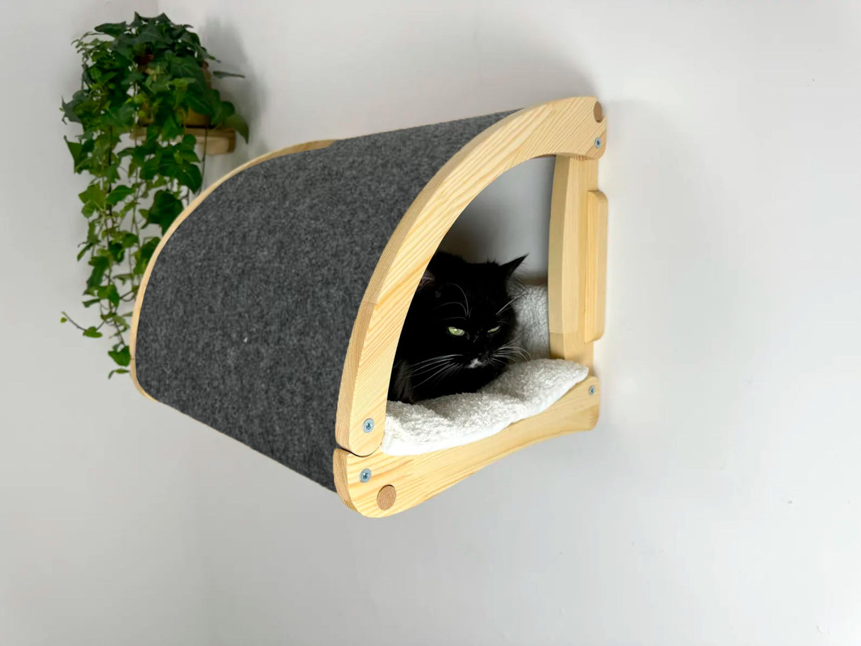 Cat lying on a wall-mounted cat bed with wooden frame and gray cushion.