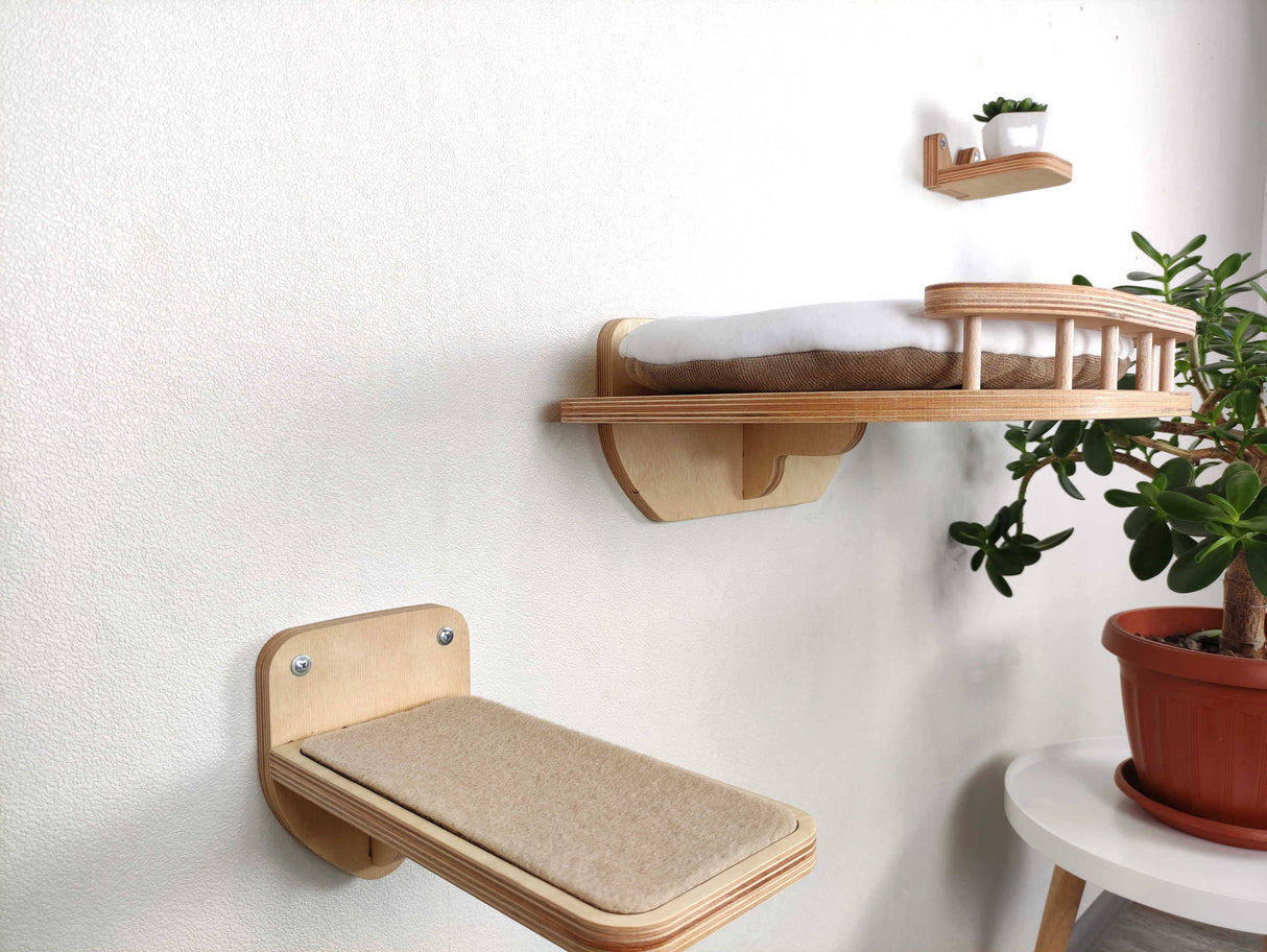 Wooden wall-mounted cat shelves with cushions on a white wall, with a plant in the corner.