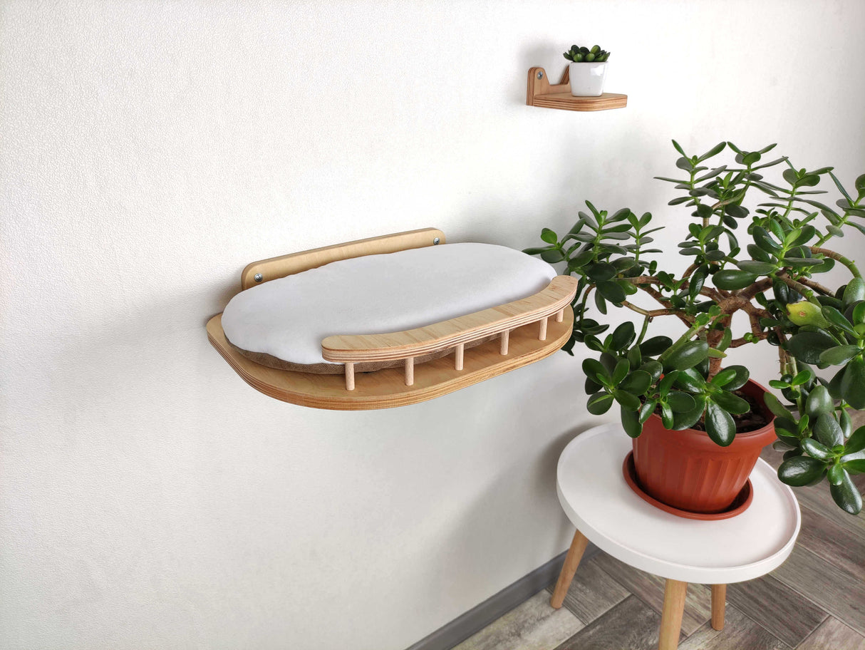 Wall-mounted cat shelf with a plant and small table against a white wall.