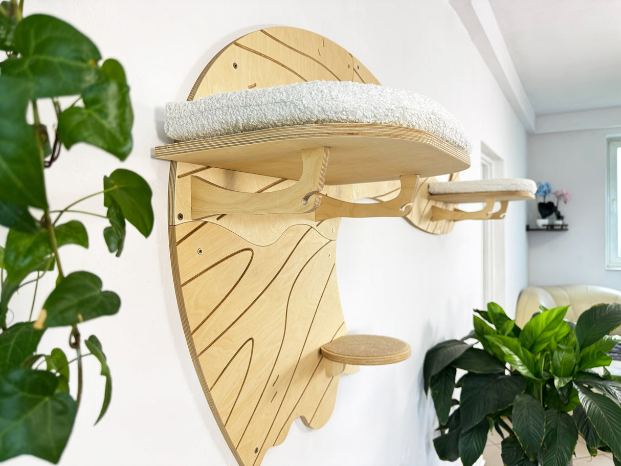 Wooden wall-mounted cat shelf with a white cushion, surrounded by green plants.