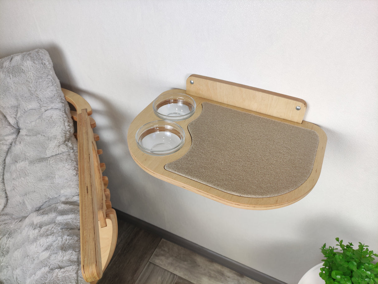 Natural wood cat shelf with beige mat and recessed feeding bowls on the left side, attached to a wall.