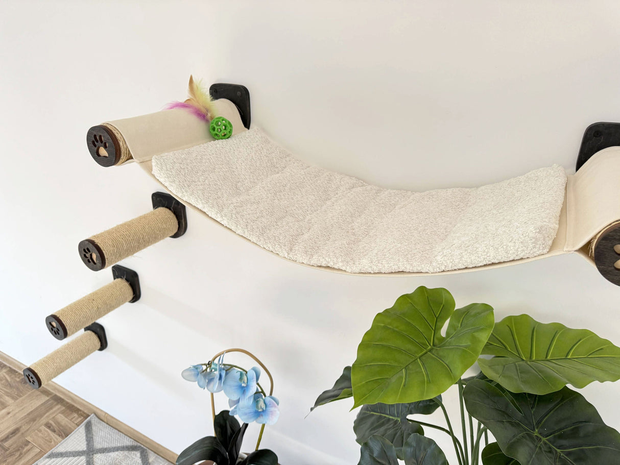 Cat climbing hammock with a white cushion and green leaves in the foreground