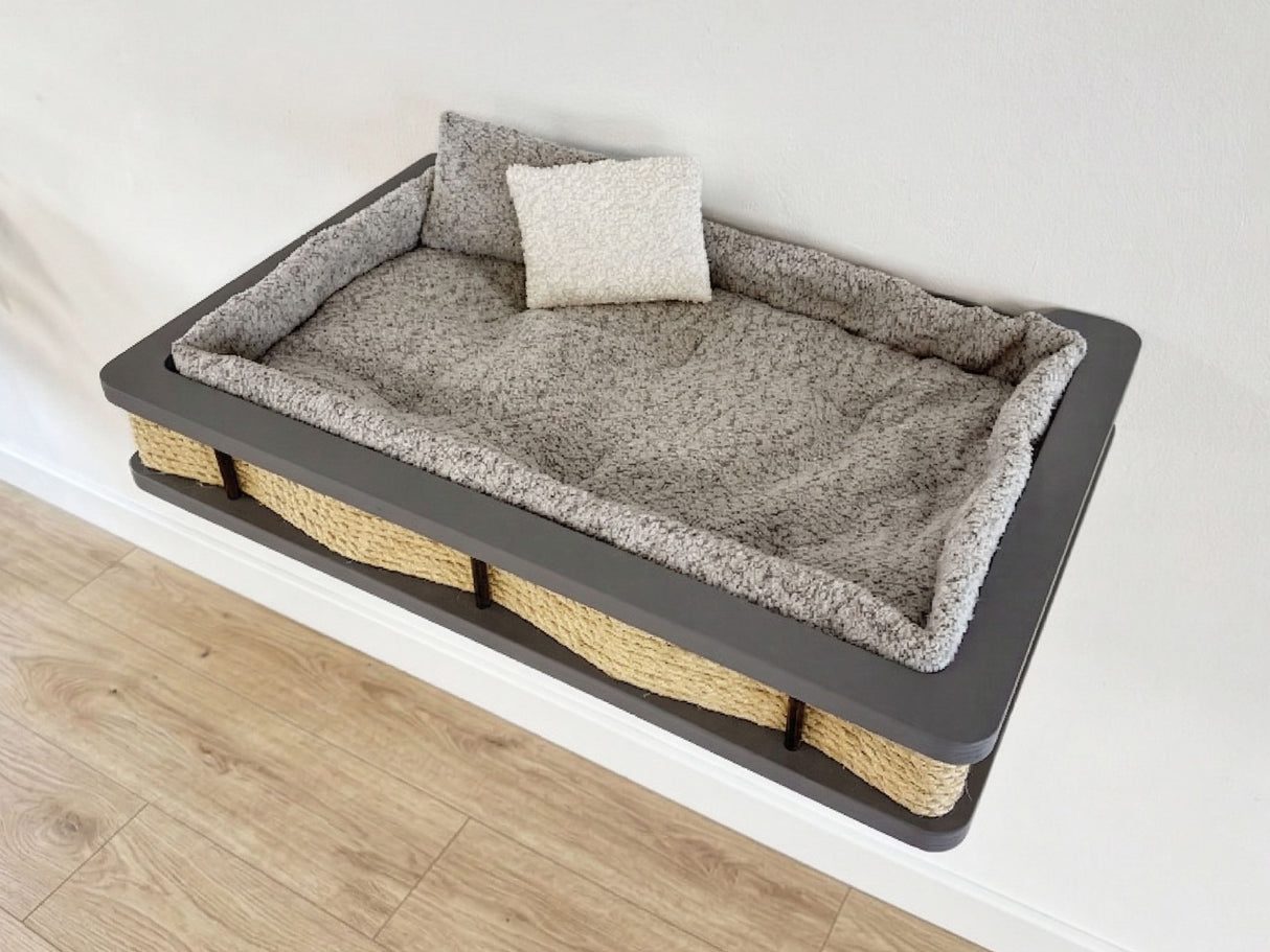 Pet bed with gray cushion and wicker base on a light wooden floor.