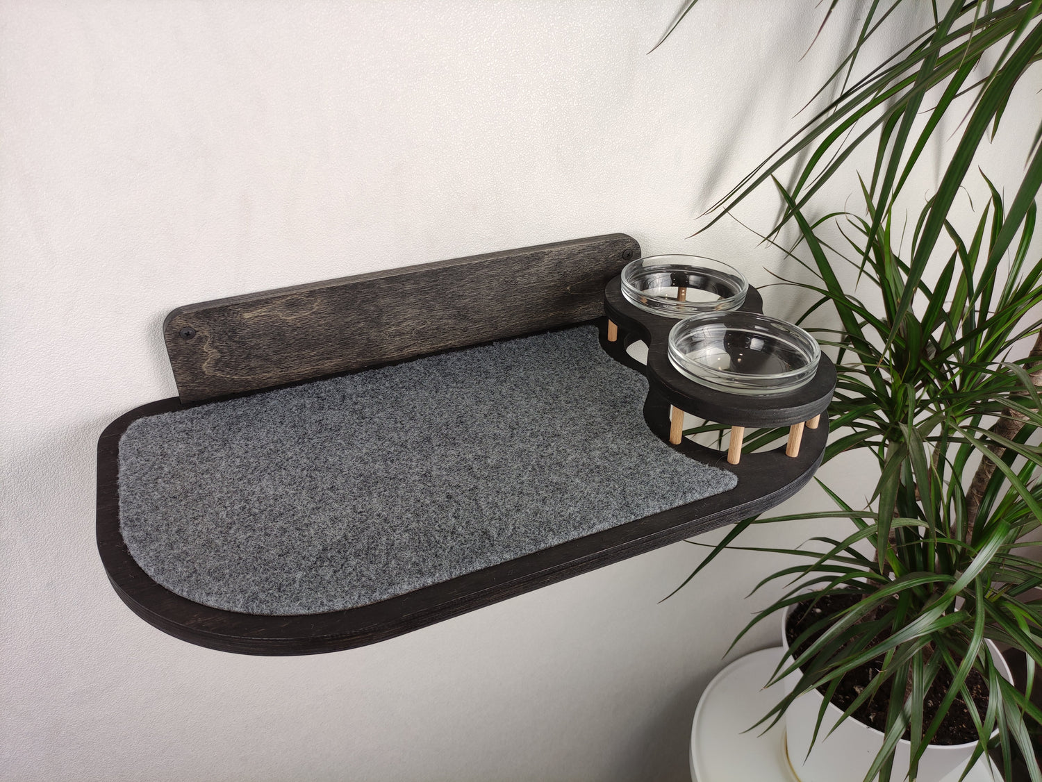Stylish dark wood cat feeding shelf with elevated glass bowls and a durable gray carpet for added comfort