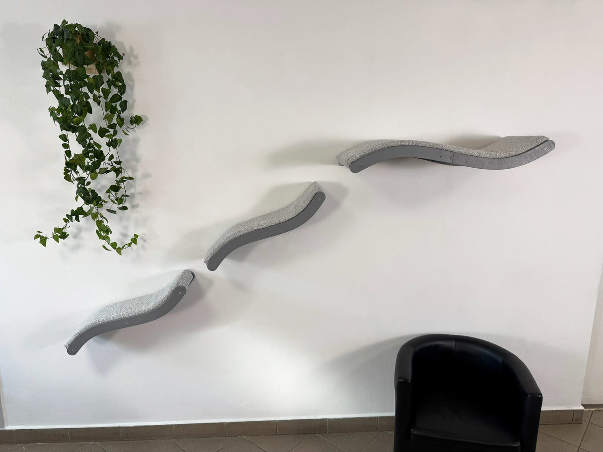 Three wavy gray wall shelves on a white wall with a plant and black chair.