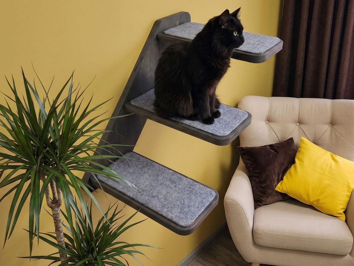 Cat sitting on a multi-level cat tree against a yellow wall with a beige sofa and decorative pillows.
