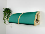 Green cylindrical cat bed with wooden frame against a white wall