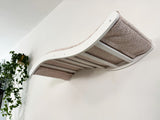 White pet shelf-bed with pale pink cushion on a white wall