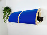 Blue cat tunnel attached to a white wall with a black cat peeking out.