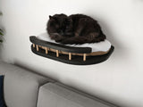 Black cat sleeping on a modern wall-mounted pet bed against a white wall.