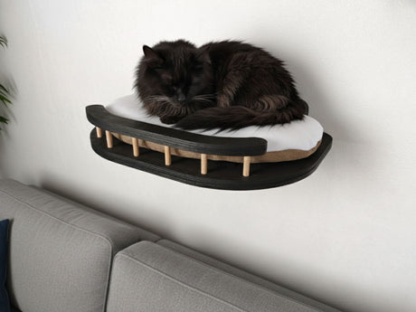 Black cat sleeping on a modern wall-mounted pet bed against a white wall.