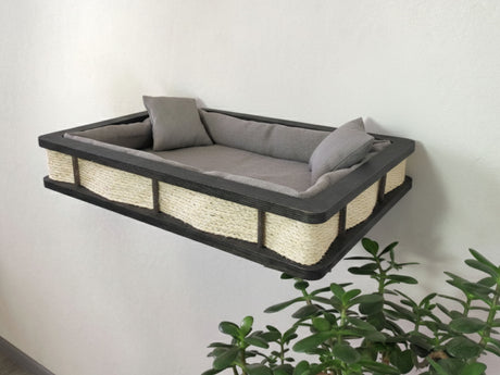 Wall-mounted cat bed with gray cushion and wooden frame against a white wall.