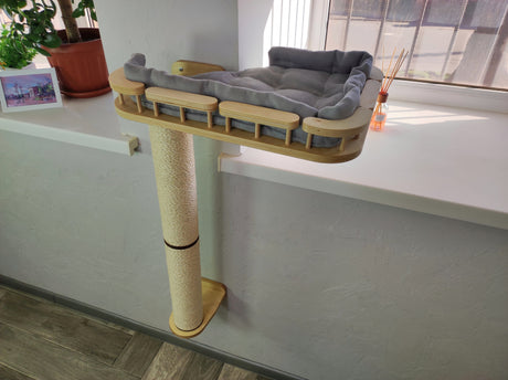 Cat tree with a platform and scratching post in a room with a window and plant.