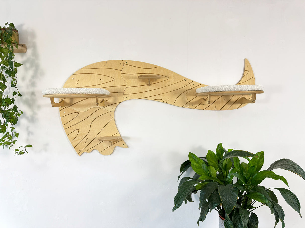 Wooden whale-shaped shelf on a white wall with plants on either side.
