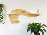Wooden whale-shaped shelf on a white wall with plants on either side.
