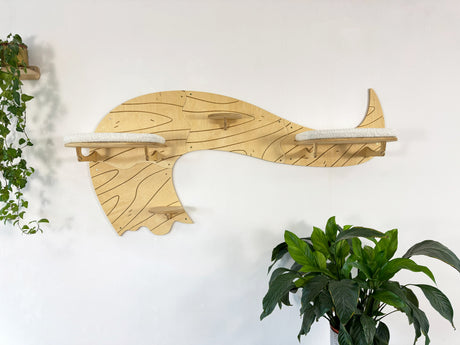 Wooden whale-shaped shelf on a white wall with plants on either side.