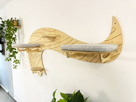 Wooden cat shelf shaped like a crescent moon with a cushion on a white wall.