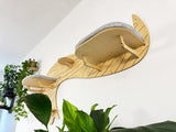 Wooden wall-mounted cat shelf with a cushion in a room with plants