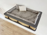 Pet bed with gray cushion and wicker base on a light wooden floor.